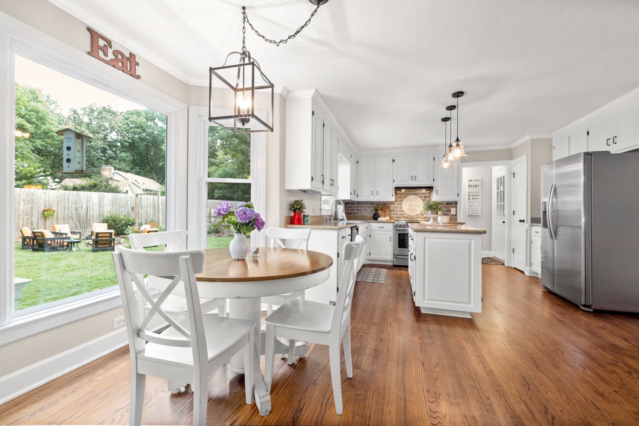 Modern kitchen with white cabinets and dining area with outdoor view.